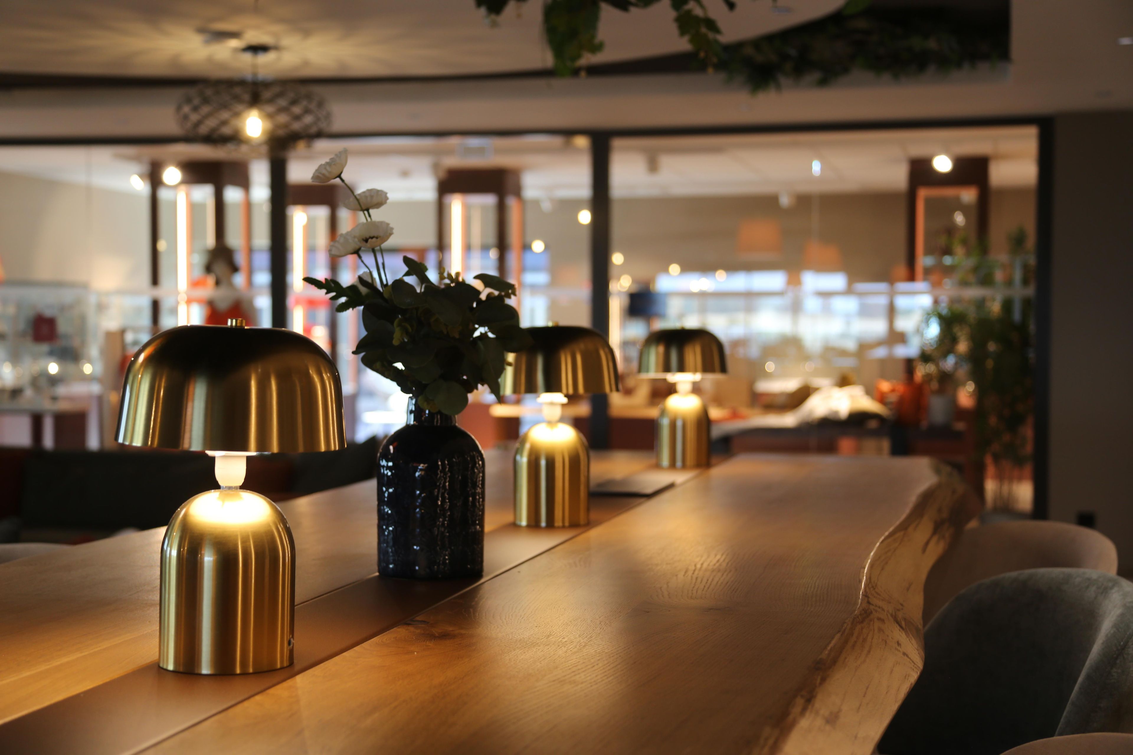 Uma longa mesa de madeira com luminárias decorativas e um vaso com flores.