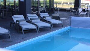 A pool area with lounge chairs and tables, a clear pool, and a view of the outdoors. - Kyriad Prestige - Sarrebourg Les Terrasses (Sarrebourg)