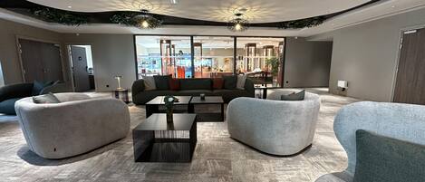 A modern living room with a sectional sofa, two armchairs, a coffee table, and a view of a retail store through large windows.