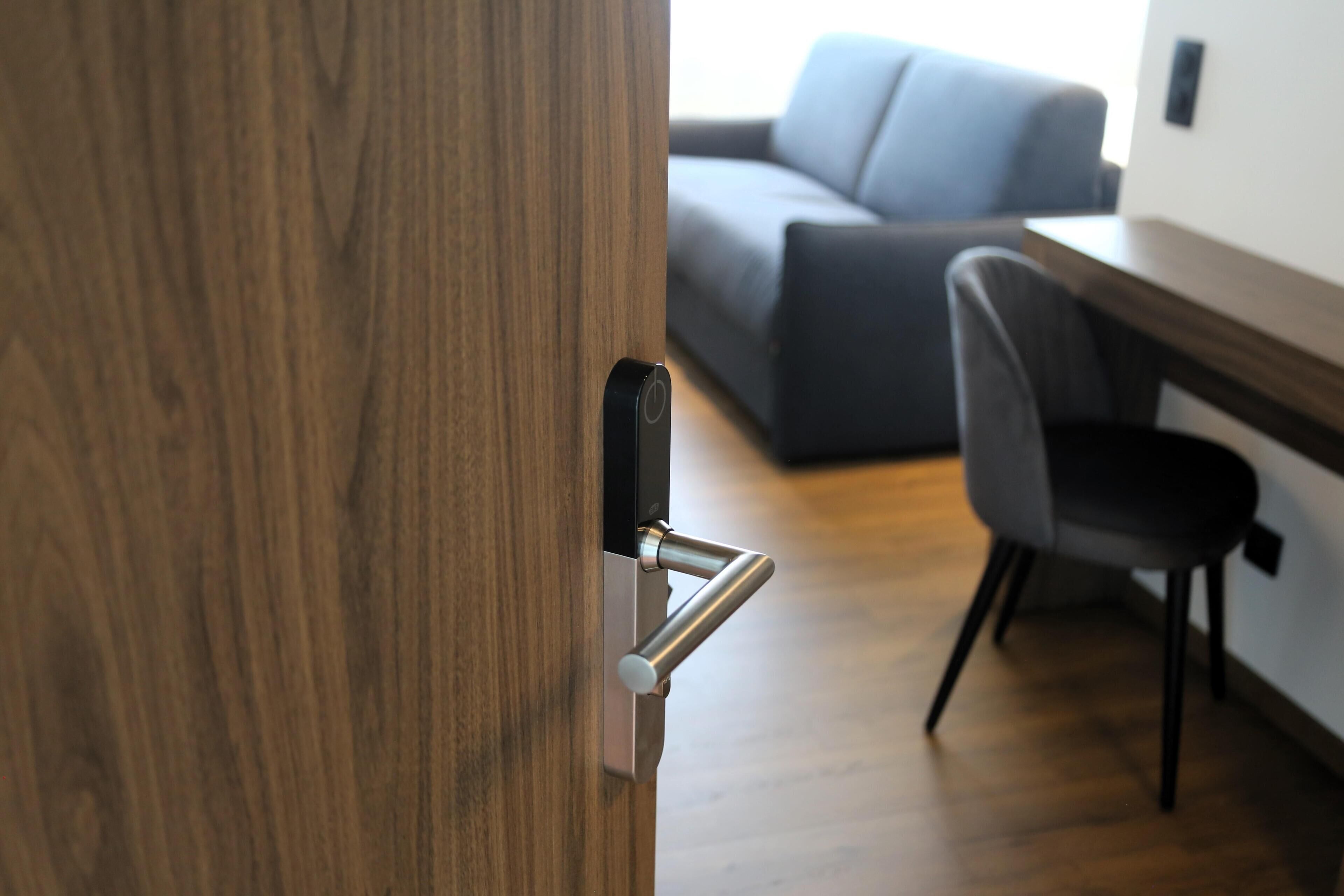 A wooden door with a modern handle, a grey office chair, and a grey sofa in the background.