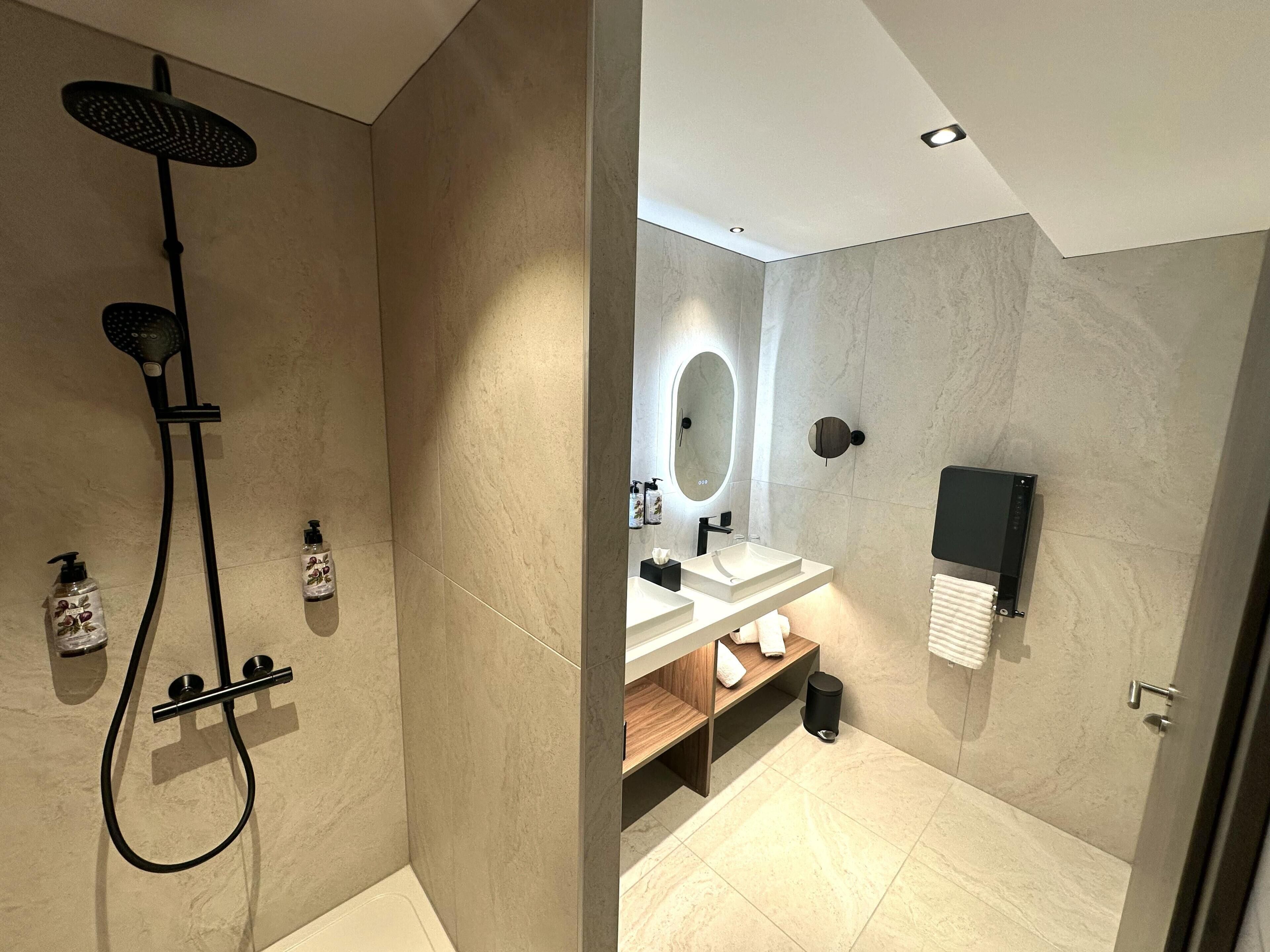 A modern bathroom with a shower, two sinks, a mirror, and a towel rack.