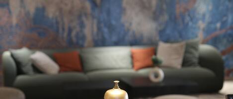 Una habitación con una mesa de madera en primer plano y un sofá verde con cojines al fondo.