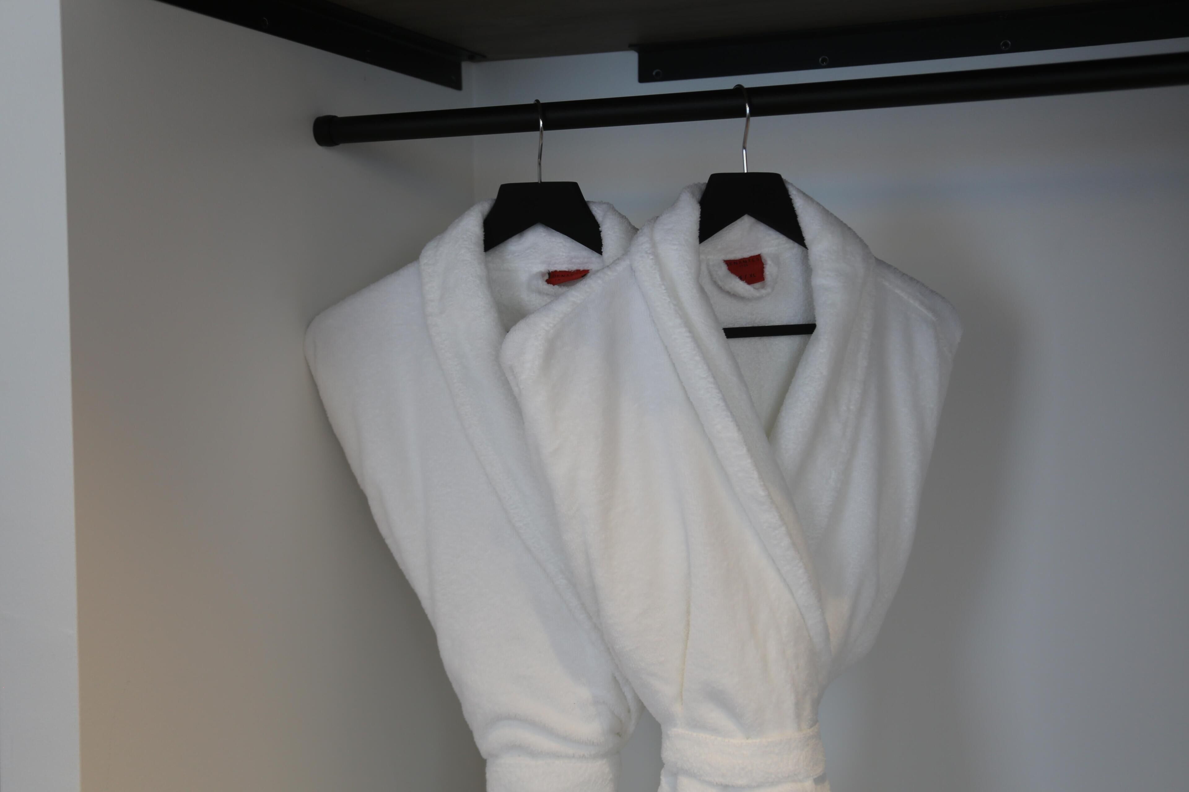 Two white robes hanging on a black hanger against a white wall.