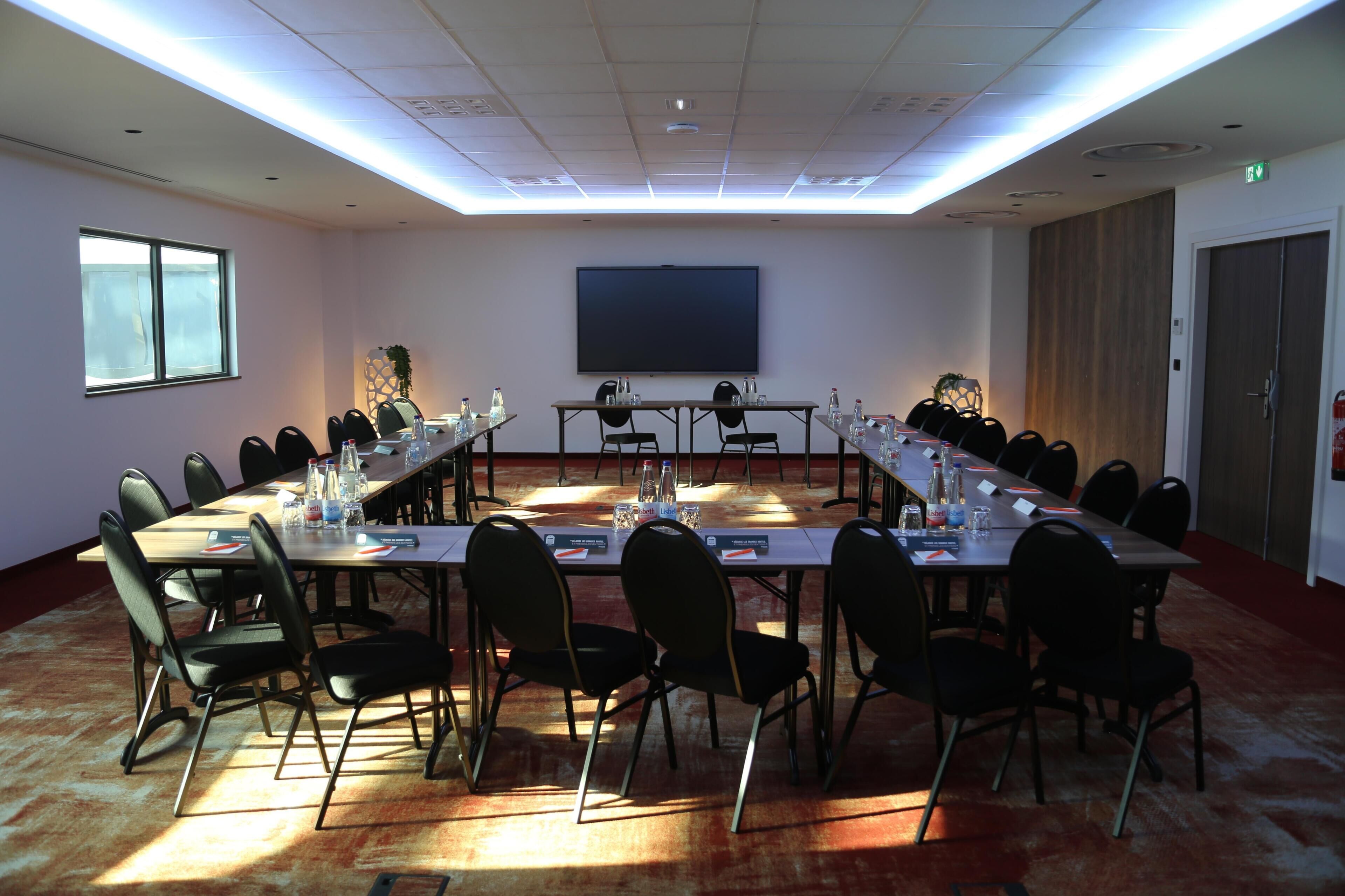 A conference room with a long table, chairs, a projector screen, and a window.