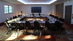 A conference room with a long table, chairs, a projector screen, and a window. - Kyriad Prestige - Sarrebourg Les Terrasses (Sarrebourg)