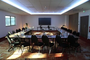 A conference room with a long table, chairs, a projector screen, and a window.