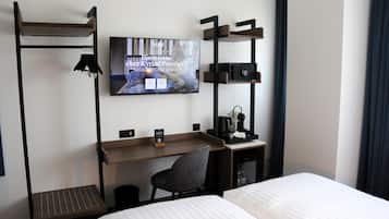 Una habitación de hotel con cama, escritorio con silla, televisor montado en la pared y un armario pequeño.