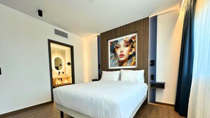 A hotel room with a large bed, a bathroom with a mirror and sink, and a painting on the wall. - Kyriad Prestige - Sarrebourg Les Terrasses (Sarrebourg)