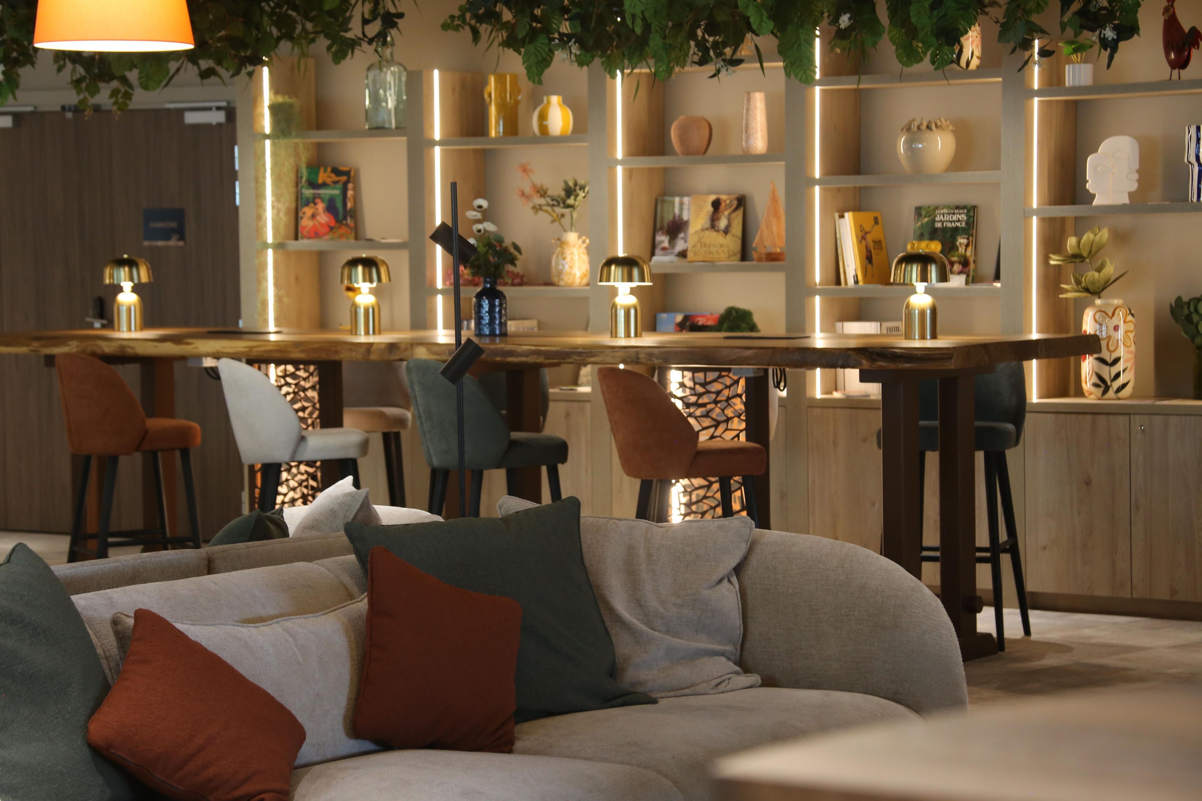 Un espace bar moderne avec un canapé et des fauteuils, un comptoir en bois et des étagères ornées d’objets décoratifs.