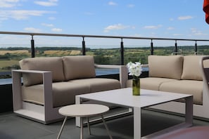 Ein Balkon mit zwei Sofas und einem kleinen Tisch, mit Blick auf eine ländliche Landschaft.
