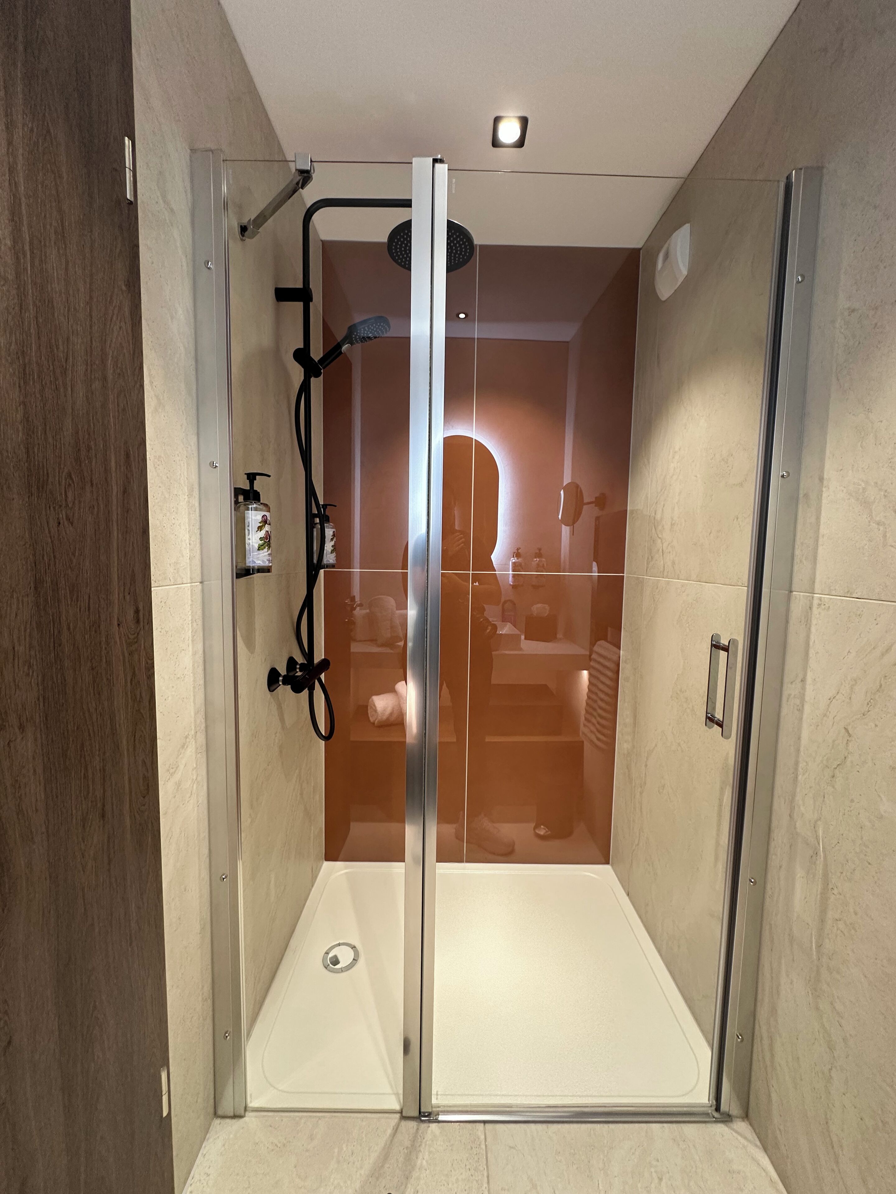 A modern bathroom with a glass-enclosed shower, a handheld showerhead, and a handheld dryer.