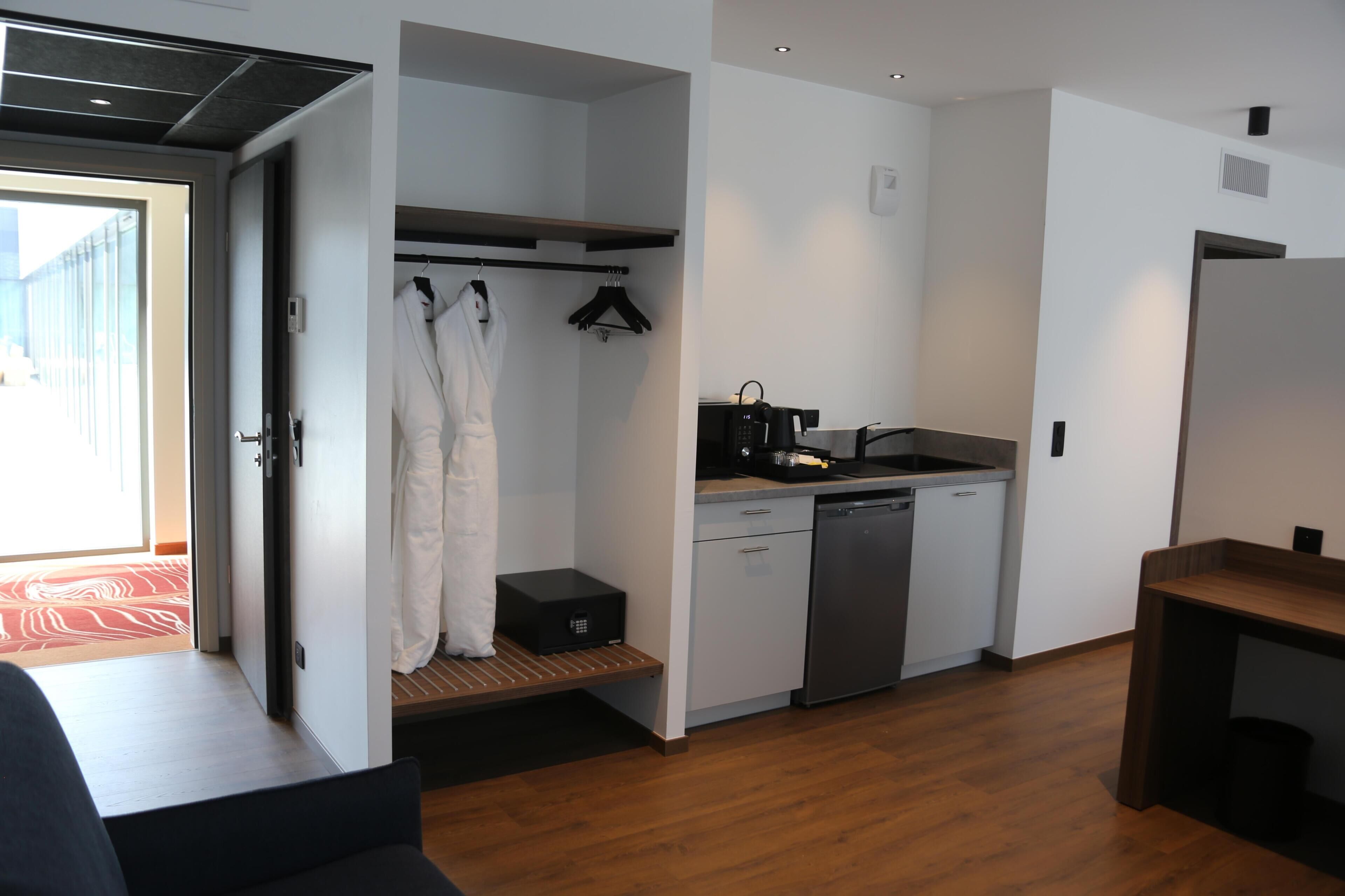 Una habitación de hotel compacta con kitchenette, un vestidor amplio y vistas a través de una puerta abierta.