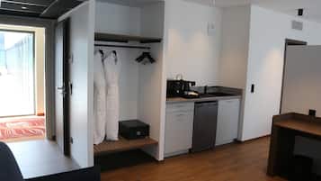 Una habitación de hotel compacta con kitchenette, un vestidor amplio y vistas a través de una puerta abierta.