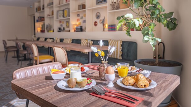 A breakfast setting with a wooden table, plates of food, a vase with flowers, and a potted plant.