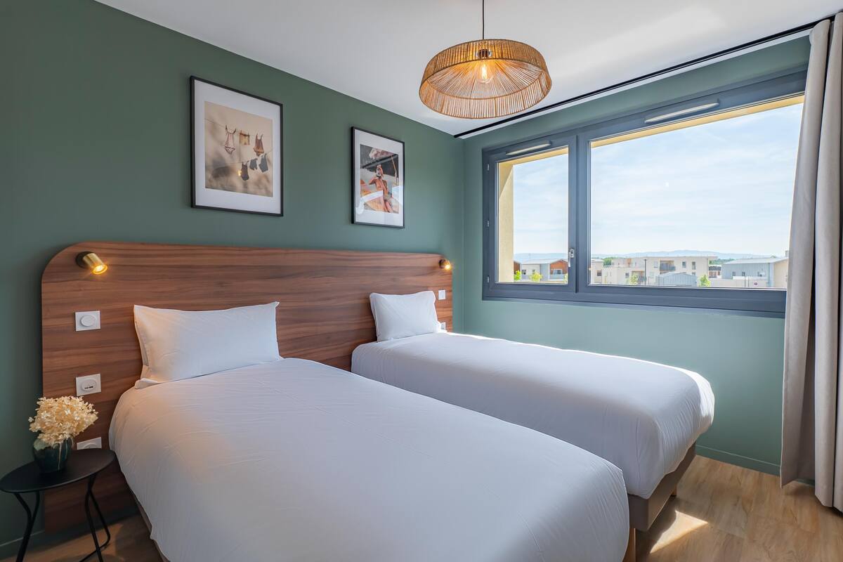 A hotel room with two beds, a wooden headboard, a large window with a view, and a hanging light fixture.