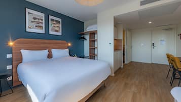 Una habitación de hotel con una cama grande, un escritorio, una silla, un armario y una kitchenette.