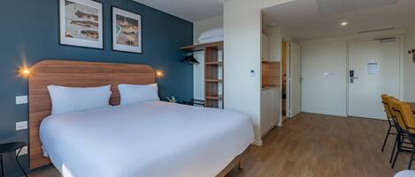Una habitación de hotel con una cama grande, un escritorio, una silla, un armario y una kitchenette.