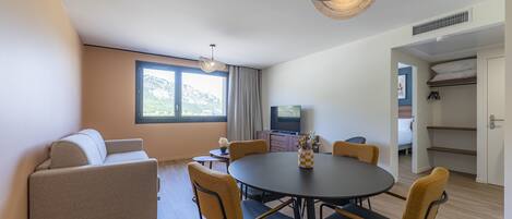 Un salon moderne comprenant un canapé, une table à manger, des chaises, un téléviseur et une grande fenêtre donnant sur une vue imprenable sur les montagnes.