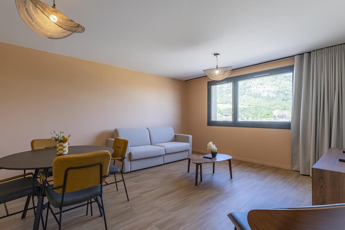 A modern living room with a sofa, dining table, chairs, a small coffee table, and a TV.