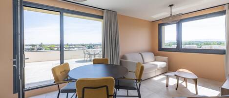 Una habitación moderna con balcón, una mesa redonda, sillas, un sofá y una mesita.