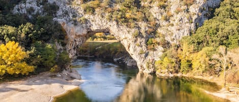 A natural rock arch over a river with surrounding greenery.