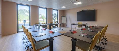 A conference room with a large table, chairs, a projector screen, and a view of the outdoors.