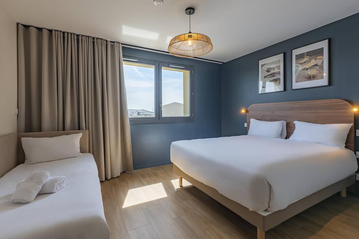 A hotel room with a bed, a sofa, a window, and a wall-mounted light fixture.