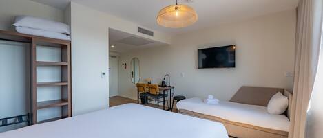 A hotel room with two beds, a desk with chairs, a television, and a large window.