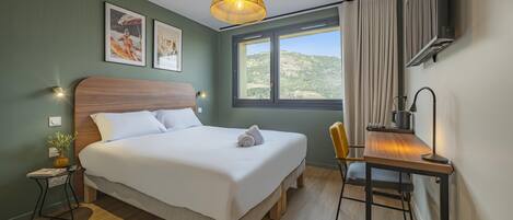 A neatly arranged hotel room with a bed, bedside table, lamp, and a view of the outdoors.
