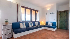 Una sala de estar con un sofá azul, almohadones blancos, una pequeña mesa con una planta y una lámpara.