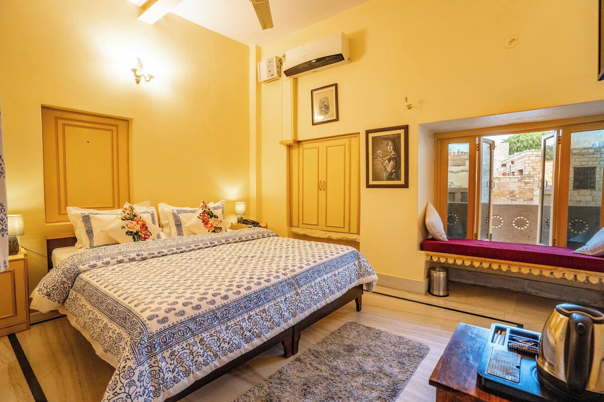 Un dormitorio con una cama grande, una ventana con vistas, una mesita con una tetera y un radiador.