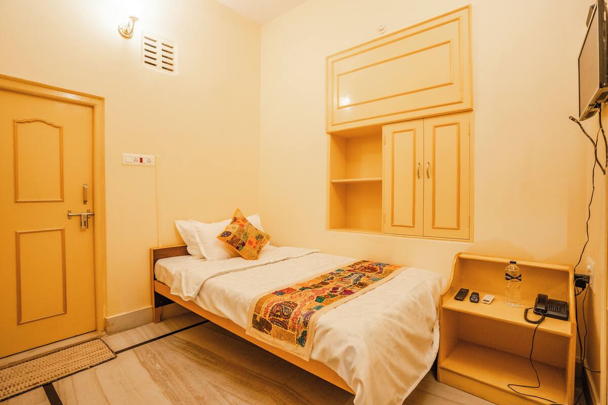 Una habitación pequeña con una cama individual, una mesita de noche con un teléfono y una botella, y un armario empotrado.