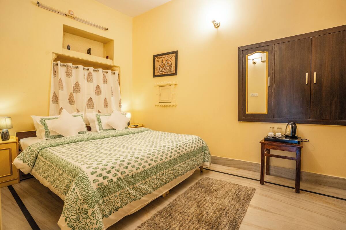 Un dormitorio con cama, mesitas de noche, un espejo, una estantería con objetos decorativos y una lámpara de pared.