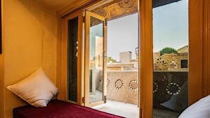 A room with a bed, a window with a view of buildings, and a door with decorative glass panels. - HOTEL HIMMAT NIWAS (Jaisalmer)