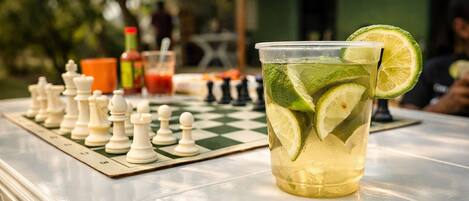 A chessboard with pieces, a glass of a lime-based drink, and a bottle of sauce on a table.