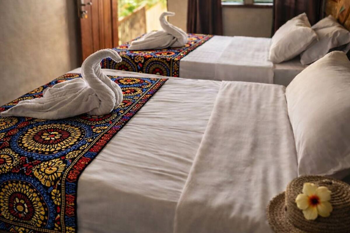 Une chambre avec deux lits, chacun surmonté d’un dais blanc et agrémenté d’une serviette décorative en forme de cygne.