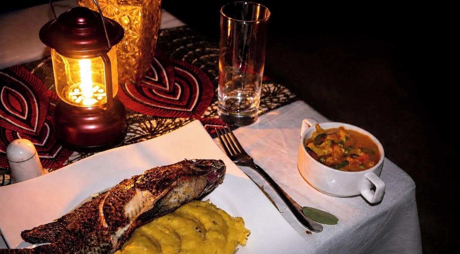 A table with a fish, mashed potatoes, and a bowl of soup.