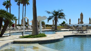 Uma área de piscina com espreguiçadeiras, palmeiras e céu claro.