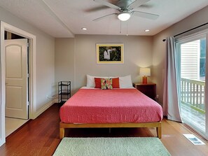 Un dormitorio con cama, ventilador de techo, ventana con cortinas y una puerta.