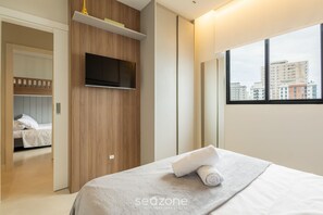 Ein modernes Hotelzimmer mit Bett, Wandfernseher und Fenster mit Blick auf die Stadt.