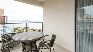 Un balcone con un tavolo rotondo e sedie in vimini, con vista su un panorama urbano che include edifici e montagne.