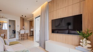 Un soggiorno moderno con una grande TV a schermo piatto montata su una parete in legno, un divano, un tavolino da caffè e un'area pranzo con tavolo e sedie.