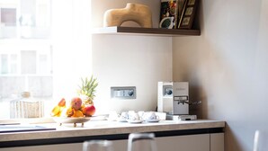 Une cuisine moderne avec un coin repas, comprenant une machine à café, un panier de fruits et des livres sur des étagères.