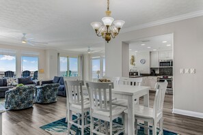 Ein geräumiges Wohnzimmer mit Essbereich, großen Fenstern und einer Küche im Hintergrund.