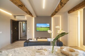 A modern living room with a marble table, a sofa, and a TV displaying a landscape. - Palazzo del Papa country Suites De luxe (Siena)