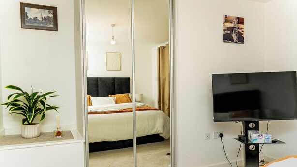 A hotel room with a bed, a TV, a plant, and a painting on the wall. - Luxury 4-Bedroom Family Home in Nuneaton Sleeps 10, Spacious, Safe & Comfortable (Nuneaton)