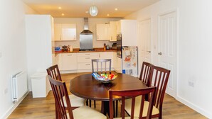 A dining area with a round table, wooden chairs, and a bowl of snacks. - Luxury 4-Bedroom Family Home in Nuneaton Sleeps 10, Spacious, Safe & Comfortable (Nuneaton)