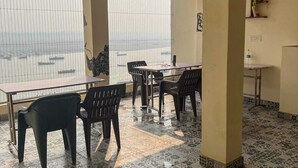 A spacious room with a tiled floor, several tables and chairs, and a large window overlooking a body of water. - NS BACKPACKERS HOSTEL (VARANASI)