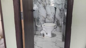 A bathroom with a toilet, marble walls, and a tiled floor. - NS BACKPACKERS HOSTEL (VARANASI)