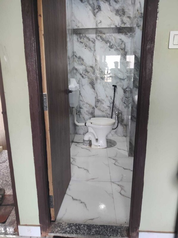 A bathroom with a toilet, marble walls, and a tiled floor. - NS BACKPACKERS HOSTEL (VARANASI)